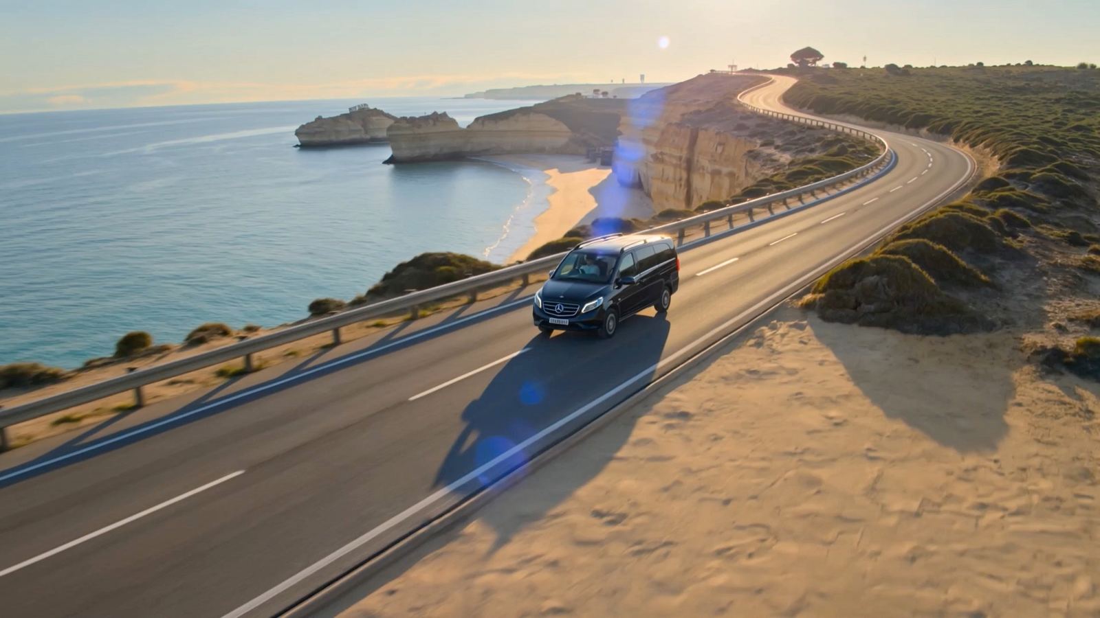 Mercedes V-Class preto numa estrada costeira sobre uma praia do Algarve ao fim da tarde