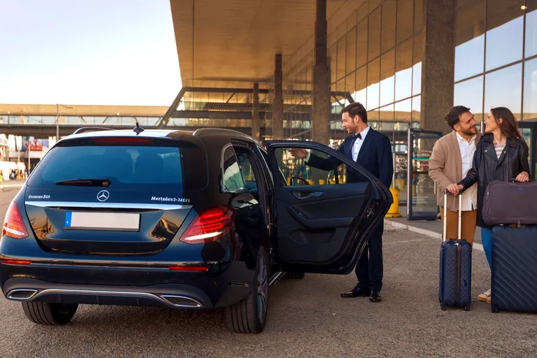 Motorista a abrir a porta de um Mercedes E-Class Estate preto a um casal à saída do aeroporto